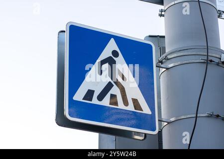 Un cartello blu e bianco di attraversamento pedonale è attaccato a un palo alto, che lo rende visibile a tutti i pedoni e conducenti nelle vicinanze Foto Stock