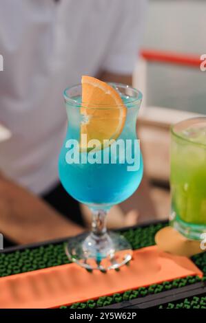 Rinfrescante cocktail Tropical Blue con contorno agrumato sul vivace bancone del bar. Foto Stock