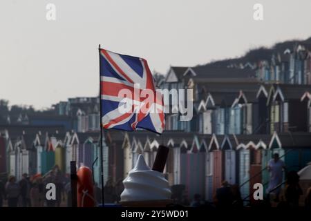 La Union Flag che vola di fronte a una linea di capanne sulla spiaggia nella località balneare di Walton-on-the-Naze nell'Essex Foto Stock