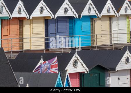 Linea di colorate capanne sulla spiaggia a Walton-on-the-Naze, Essex, con la Union Flag decorata con l'immagine di re Carlo III Foto Stock