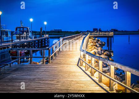 Passerella in legno illuminata sul mare dopo il tramonto all'ora blu. Molo in legno nella città tedesca di Heiligenhafen sul Mar Baltico. Copia spazio. Foto Stock