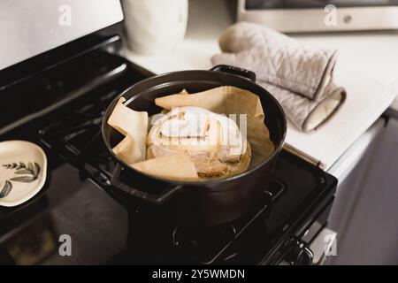 Pane a lievitazione naturale appena sfornato in un forno olandese con guanti da forno nelle vicinanze Foto Stock