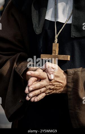 Una suora in abiti tradizionali e con una croce di legno sul petto tiene le mani in preghiera. Foto Stock