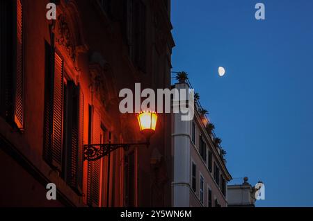 La lanterna della strada illumina i vecchi edifici al crepuscolo sotto il cielo limpido con la luna Foto Stock