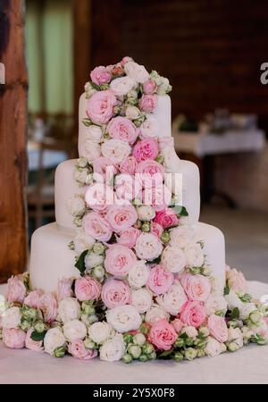 Una torta nuziale splendidamente decorata adornata con rose rosa e bianche in un ambiente interno rustico. Foto Stock