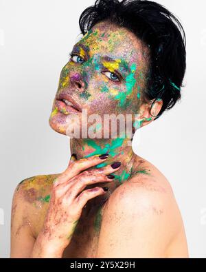 Donna con vernice colorata si schizza sul viso e sul corpo in posa su uno sfondo bianco. Foto Stock