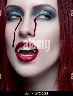 Donna con i capelli rossi e un trucco spettacolare, compreso il rossetto rosso macchiato Foto Stock