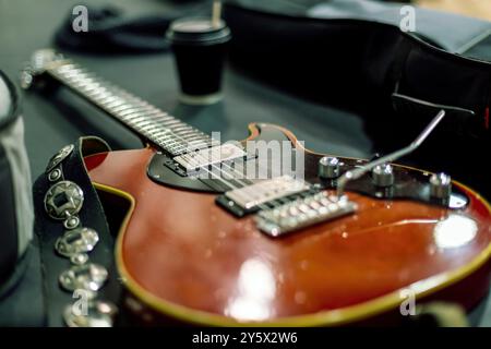 Primo piano di una chitarra elettrica rossa su un tavolo con sfondo sfocato con cappello nero e tazzina da caffè da asporto. Foto Stock