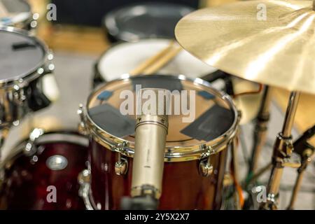 Primo piano di un microfono davanti a un gruppo di tamburi con un piatto, che mostra una registrazione musicale o una configurazione delle prestazioni. Foto Stock