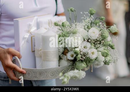 Una persona che regge un vassoio decorativo con fiori bianchi, candele e una confezione regalo per le occasioni speciali. Foto Stock