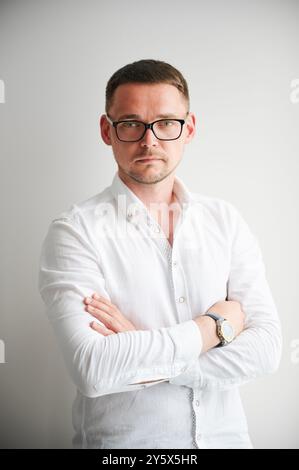 Ritratto di un uomo con un'espressione seria e sicura sul suo volto. Bel giovane uomo in abiti casual che tiene le braccia incrociate mentre sta in piedi su sfondo bianco. Foto Stock