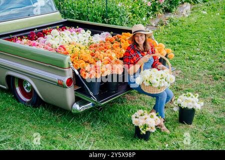 Donna sorridente in un cappello che organizza mazzi di fiori colorati sul retro di un pick-up d'epoca in una giornata di sole. Foto Stock