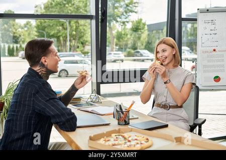 Due giovani colleghi condividono un momento di luce con la pizza durante la pausa di mezzogiorno al lavoro. Foto Stock