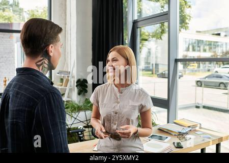 Due colleghi condividono una discussione amichevole in un ufficio moderno pieno di luce naturale. Foto Stock