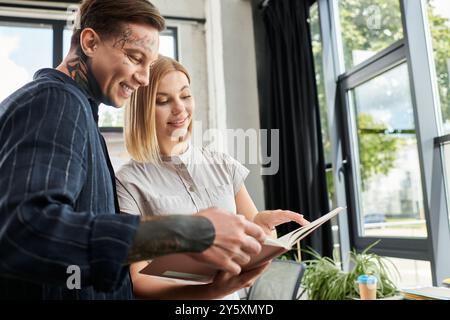 Due giovani professionisti condividono le idee con entusiasmo durante la revisione dei documenti in ufficio. Foto Stock