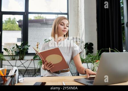 Un membro del team attento esamina gli appunti mentre si interagisce con un notebook in un ambiente di ufficio vivace. Foto Stock