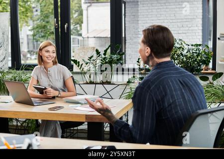 Due giovani professionisti condividono idee e collaborano in uno spazio di lavoro luminoso e pieno di piante. Foto Stock