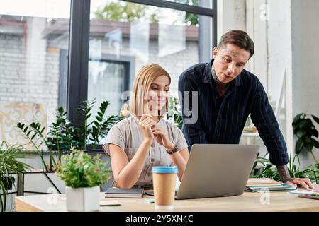 Due colleghi impegnati discutono idee e rivedono il lavoro sul proprio notebook in un ufficio vivace. Foto Stock