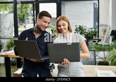 Due giovani colleghi condividono idee mentre lavorano su notebook in un ufficio luminoso e vivace. Foto Stock