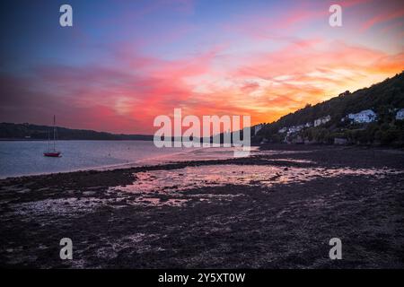 Uno yacht a vela solitario al tramonto rosso sopra lo stretto di Menai tra Anglesey, Yns Mon e Bangor sulla terraferma del Galles del Nord. Foto Stock