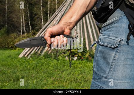 Coltello di sopravvivenza pieghevole nelle mani di un uomo forte in natura. Foto in primo piano. Foto Stock