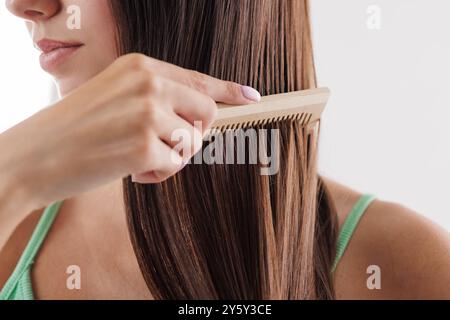 Primo piano di una donna che pettina i suoi lunghi capelli castani dritti con un pettine di legno. cura dei capelli, problema dei capelli Foto Stock