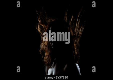 Questa straordinaria immagine cattura la silhouette di una donna con i suoi capelli accesi e fluenti, su uno sfondo scuro, evocando emozioni e. Foto Stock