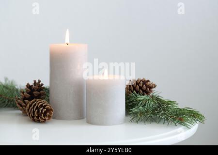 Bruciare candele e rami di abete sul tavolino da caffè vicino alla parete luminosa, spazio per il testo. Atmosfera natalizia Foto Stock