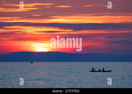 Un vibrante tramonto arancione sull'oceano con una canoa nell'acqua calma. Foto Stock