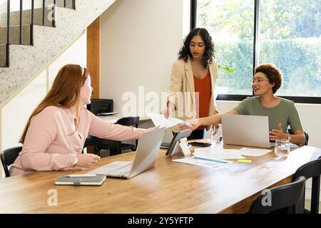 Collaborando al progetto, diverse donne e amici che utilizzano laptop e condividono documenti a tavola Foto Stock