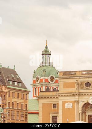 Primo piano della cupola della chiesa di Riddarholmen con tetto verde in rame e orologio, incorniciato da edifici storici di Stoccolma sotto un cielo nuvoloso Foto Stock