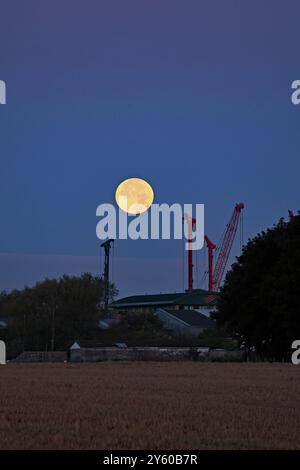 La luna del raccolto sta precipitando mentre il nuovo giorno sta per sorgere sopra il Lancashire occidentale e la zona industriale di Burscough. Foto Stock