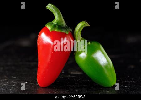 Primo piano di due peperoncini caldi, uno rosso e uno verde jalapeno affiancati, isolati su sfondo nero Foto Stock