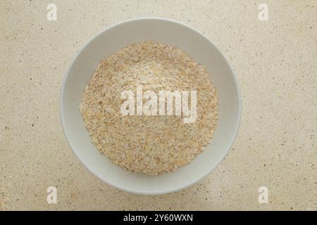 Vista dall'alto fiocchi d'avena nella ciotola bianca, colazione veloce e salutare su un tavolo di marmo bianco Foto Stock