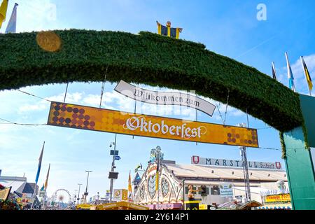 Monaco di Baviera, Germania - 23 settembre 2024: L'arco verde con l'iscrizione Welcome to Oktoberfest e la targa Oktoberfest appesa sotto di esso segna l'ingresso ufficiale al festival. Sull'arco si trova la figura del Münchner Kindl, il simbolo di Monaco, che accoglie i visitatori *** Der Grüne Torbogen mit der Aufschrift: Willkommen zum Oktoberfest und der darunter hängenden Tafel Oktoberfest markiert den offiziellen Eingang zum Festgelände. Auf dem Bogen steht die Figur des Münchner Kindls, des Wahrzeichens von München, das die Besucher begrüßt Foto Stock