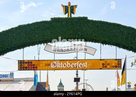 Monaco di Baviera, Germania - 23 settembre 2024: L'arco verde con l'iscrizione Welcome to Oktoberfest e la targa Oktoberfest appesa sotto di esso segna l'ingresso ufficiale al festival. Sull'arco si trova la figura del Münchner Kindl, il simbolo di Monaco, che accoglie i visitatori *** Der Grüne Torbogen mit der Aufschrift: Willkommen zum Oktoberfest und der darunter hängenden Tafel Oktoberfest markiert den offiziellen Eingang zum Festgelände. Auf dem Bogen steht die Figur des Münchner Kindls, des Wahrzeichens von München, das die Besucher begrüßt Foto Stock