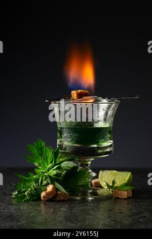 Bruciare lo zucchero su un bicchiere con assenzio. Preparazione della bevanda. Absinthe con ingredienti su sfondo nero. Foto Stock