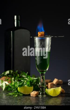 Bruciare lo zucchero su un bicchiere con assenzio. Preparazione della bevanda. Absinthe con ingredienti su sfondo nero. Foto Stock