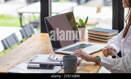 Una giovane donna d'affari sta esaminando i risultati della rete aziendale tramite computer portatili e Internet al fine di preparare documenti per le riunioni da offrire agli investitori Foto Stock