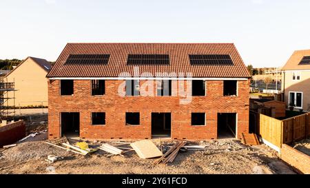 Una fila di case di nuova costruzione parzialmente costruite in un cantiere con tetto integrato o pannelli solari integrati nel tetto per un'energia economica e sostenibile in una e Foto Stock