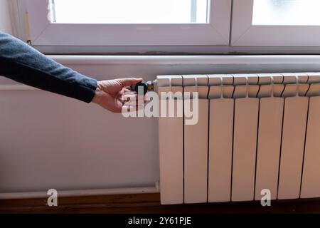 Vista rifilata del termostato manuale sul radiatore di riscaldamento bianco. Consumo di risorse naturali, risparmio energetico e concetto di casa calda Foto Stock