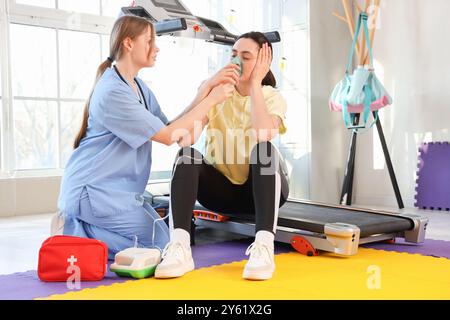 Medico donna con nebulizzatore che dà il primo soccorso alla giovane donna in palestra Foto Stock