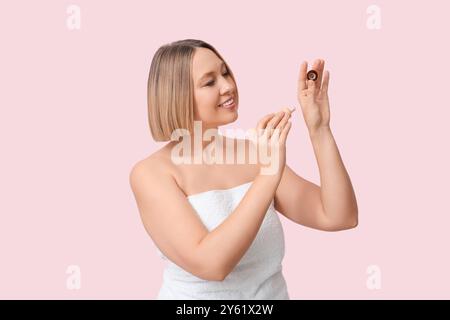 Bella donna matura dopo la doccia, che applica il fondamento per il trucco sulla mano su sfondo colorato Foto Stock