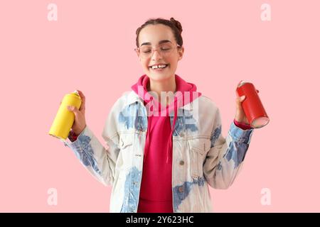 Giovane donna con bombolette di vernice spray su sfondo rosa Foto Stock