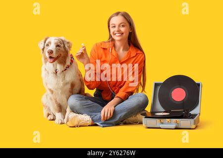 Giovane donna con auricolari con cane pastore australiano e lettore di dischi su sfondo giallo Foto Stock