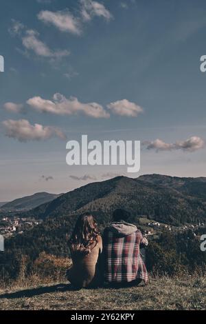 Tutte le preoccupazioni sono volate via... Vista posteriore di giovani coppie che ammirano la vista mentre si siede sulla cima della montagna Foto Stock