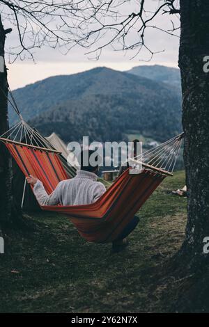 Posto perfetto in cui soggiornare. Vista posteriore del giovane seduto sull'amaca mentre campeggiava con la sua ragazza Foto Stock