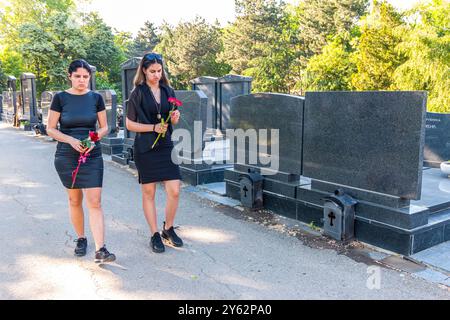 Madre e sua figlia in lutto, in abiti neri, in possesso di un fiore e in lutto per una persona cara defunta al cimitero Foto Stock