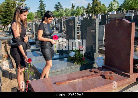 Madre e sua figlia in lutto, in abiti neri, in possesso di un fiore e in lutto per una persona cara defunta al cimitero Foto Stock