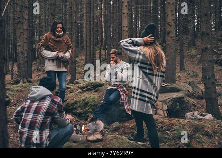 Amici per sempre. Gruppo di giovani felici in piedi intorno al fuoco mentre camminano nei boschi Foto Stock